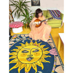 A vibrant area rug featuring a bold sun design in yellow and blue, perfect for adding a touch of whimsy to any living room. The wool rug is laid out in a cozy space with a woman playing a string instrument, surrounded by eclectic decor.