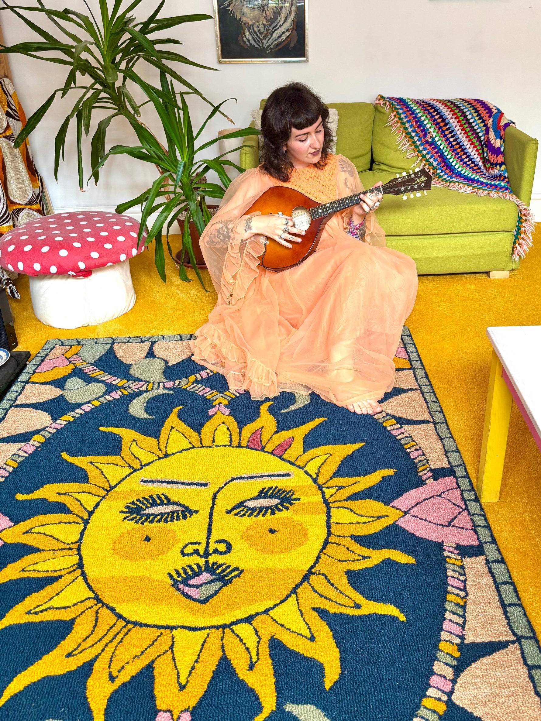 Woman playing a mandolin in a living room with a colorful rug featuring a sun design.