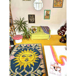 A vibrant Solstice Dreams Hand Tufted Area Rug featuring a colorful abstract sun design. This wool rug adds a lively touch to the living room, complementing the eclectic decor with a green couch, lush plants, and a cozy atmosphere.