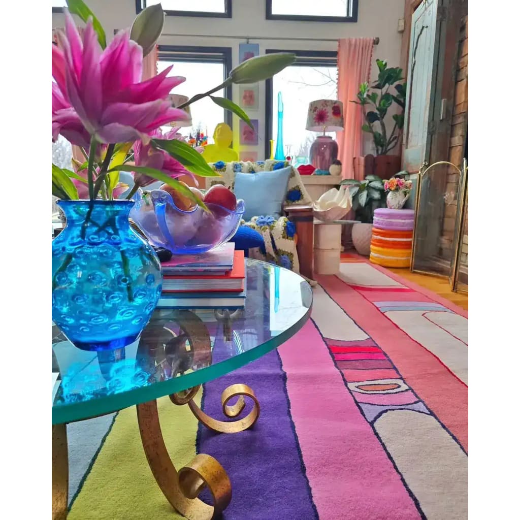 A vibrant Spectrum Stripe Hand Tufted Rug in a living room setting, showcasing its bold and colorful stripes. This contemporary wool rug adds a splash of color, complementing the eclectic decor with a glass coffee table and floral arrangements. Perfect for those seeking large living room rugs or an 8x10 area rug to enhance their space.