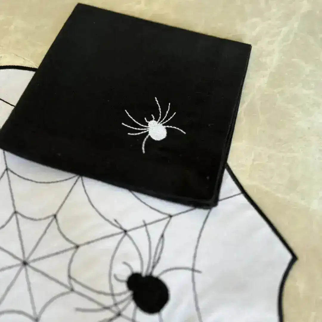 Spiderweb placemat close-up, black napkin with white embroidered spider resting on white mat with black spiderweb stitching