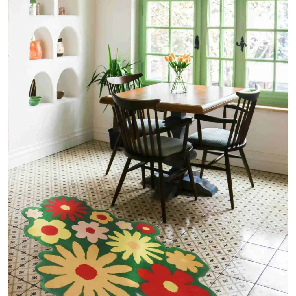 A vibrant wool area rug featuring spring flowers in a green field design, placed in a cozy office setting with a wooden table and chairs. The office rug adds a touch of nature-inspired charm to the room.