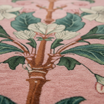 Close-up of a floral patterned rug with green leaves and brown stems on a pink background.