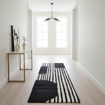 Modern hallway with a black and white striped rug, a small table with decor items, and a pendant light.