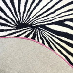 Close-up view of the Step onto the Pink Sun Hand Tufted Wool Rug, showcasing its artistic black and white abstract pattern, perfect for large living room spaces. This vintage rug features a pop of pink along the edge, adding a stylish touch to any area rug setting.