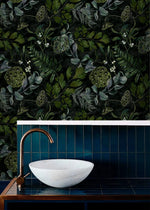 Stone basin and copper tap on blue tile below enigmatic leafy canopy wallpaper of dark leaves