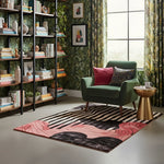 Green armchair with colorful cushions in a room with bookshelves, an abstract hand made rug, and a window.