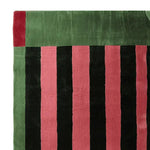 Close-up view of the Structured Red Rhythm Hand Tufted Rug showcasing its bold black and red stripes with green accents. Perfect as an area rug, this contemporary wool rug adds a vibrant touch to any living room.