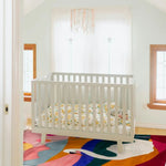 A stylish wool area rug with a vibrant swan design placed in a cozy room with a white crib. Ideal for adding a touch of elegance to a living room, dining room, or as a dining table rug. This 8x10 square rug features bold colors, making it a standout piece for any space.