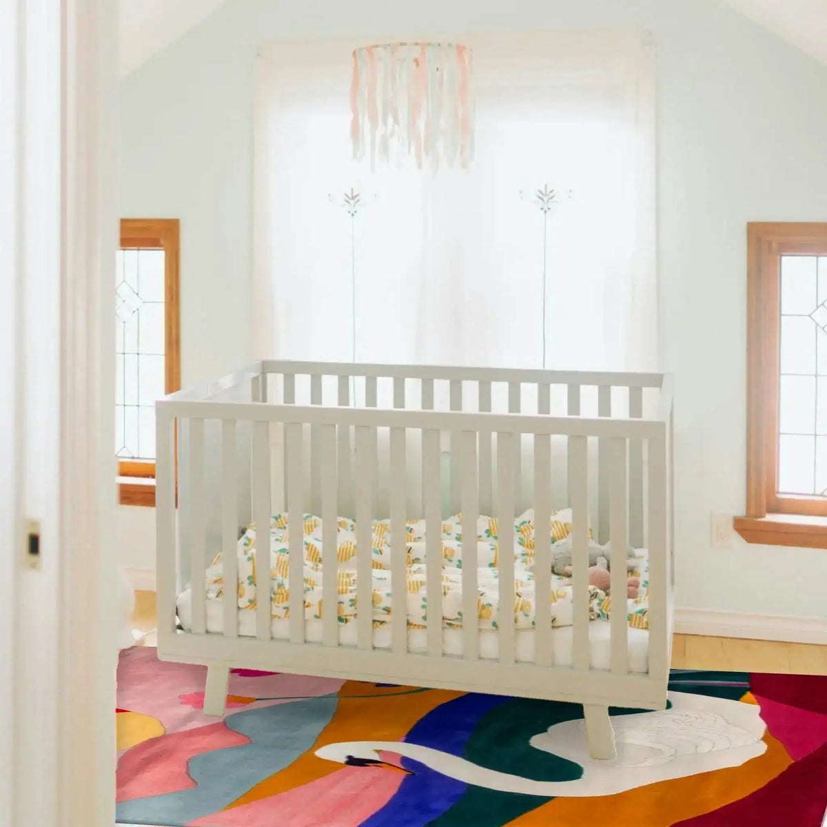 A stylish wool area rug with a vibrant swan design placed in a cozy room with a white crib. Ideal for adding a touch of elegance to a living room, dining room, or as a dining table rug. This 8x10 square rug features bold colors, making it a standout piece for any space.
