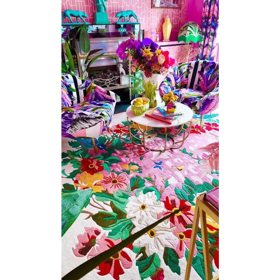 Vibrant living room featuring a Sunrise Bloom Hand Tufted Round Rug with a bold floral design. This wool rug adds a splash of color with its intricate patterns of pink, red, and green flowers, making it a perfect centerpiece for large area rugs in a living room setting. Surrounded by colorful chairs and a stylish coffee table, this round rug enhances the aesthetic of rugs for living room spaces.