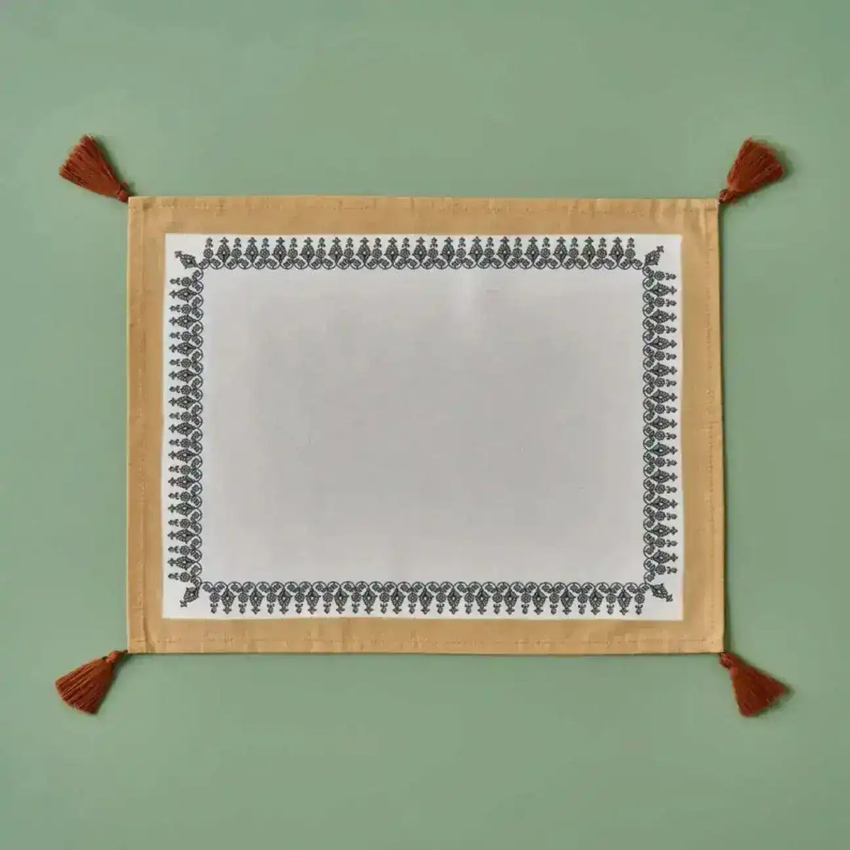 Tassel Trimmed placemat with white center, black ornate border, gold backing, rust corner tassels, flat lay