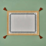 Tassel Trimmed placemat with white center, black ornate border, gold backing, rust corner tassels, flat lay
