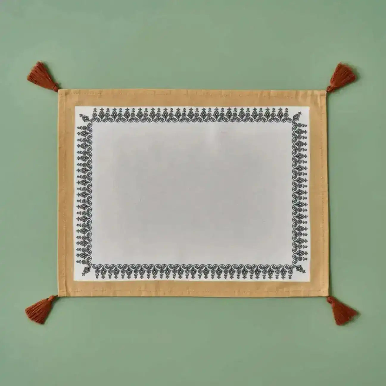 Tassel Trimmed placemat with white center, black ornate border, gold backing, rust corner tassels, flat lay