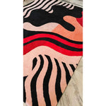 Colorful abstract patterned rug with black, red, and pink colors on a neutral background.