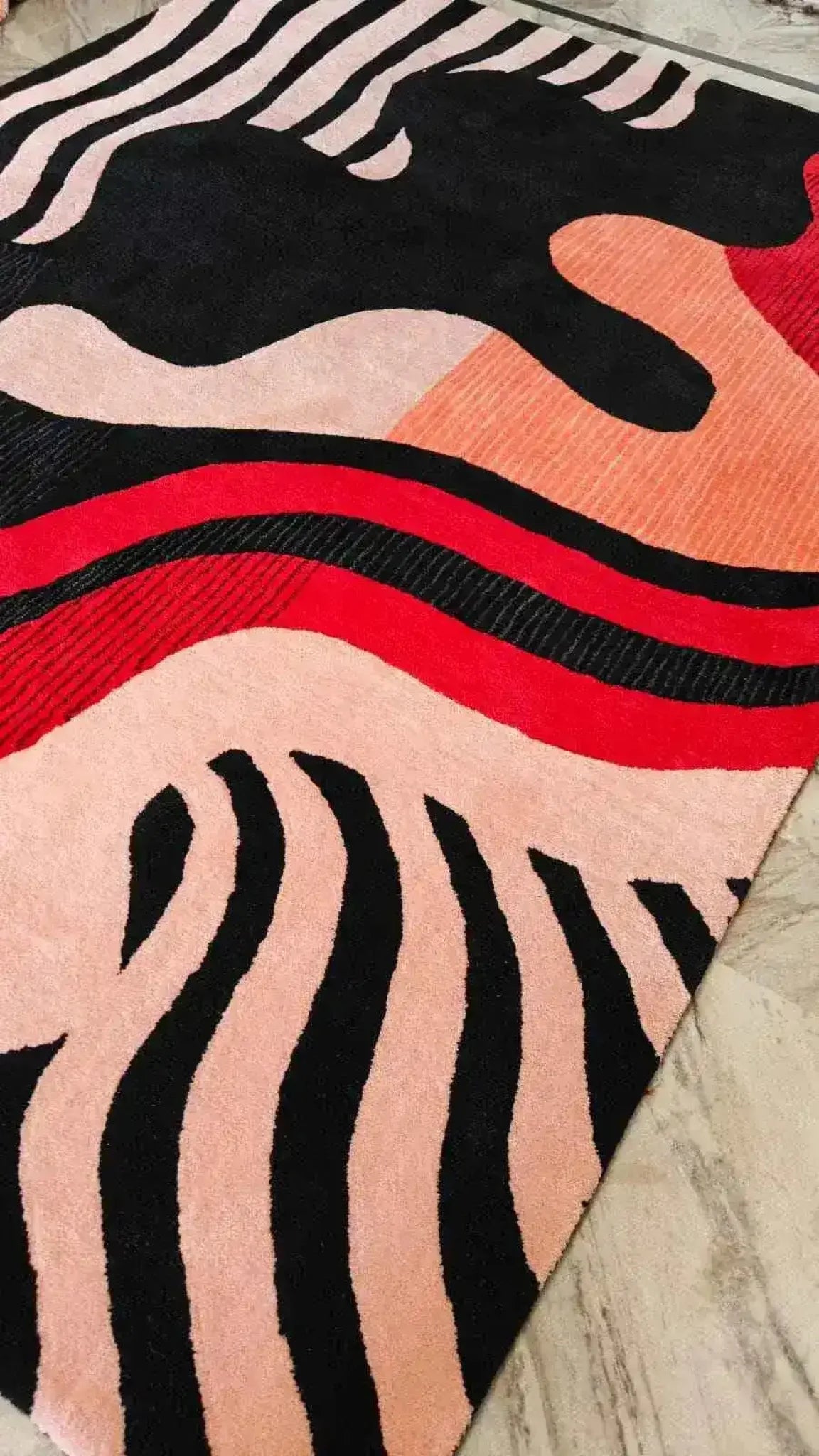 Colorful abstract patterned rug with black, red, and pink colors on a neutral background.