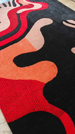 Colorful abstract patterned rug with red, black, and orange colors on a wooden floor.