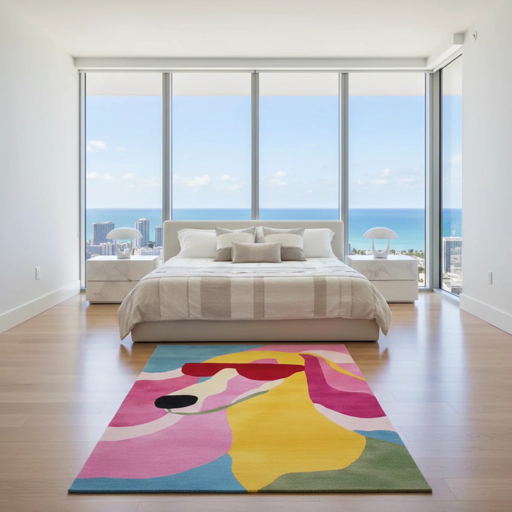 Modern bedroom with a colorful abstract rug on a wooden floor, large windows with ocean view.
