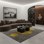 A modern living room featuring a curved brown sectional sofa, a black coffee table, a patterned rug with yellow and black abstract shapes, and a large black-and-white framed wall art piece depicting a lone figure in a mountain landscape.