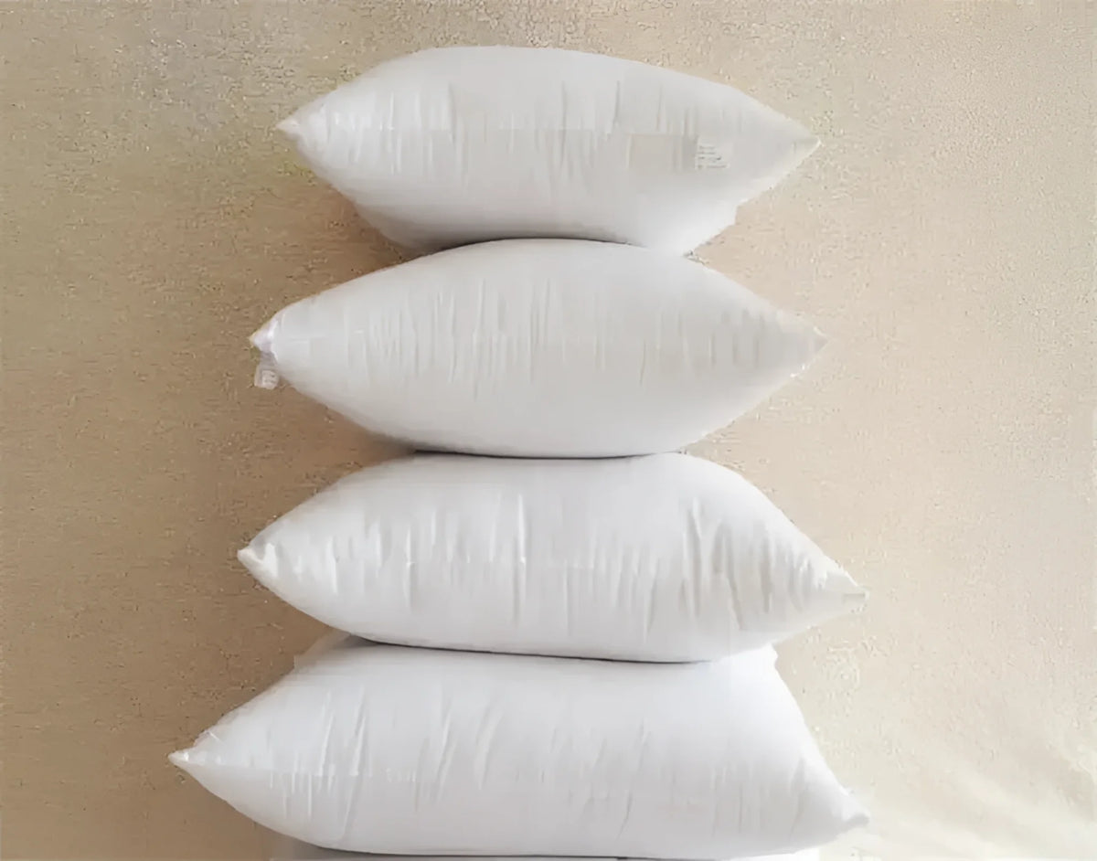 Stack of four white throw pillows on a beige surface, ideal for home decor and comfort.