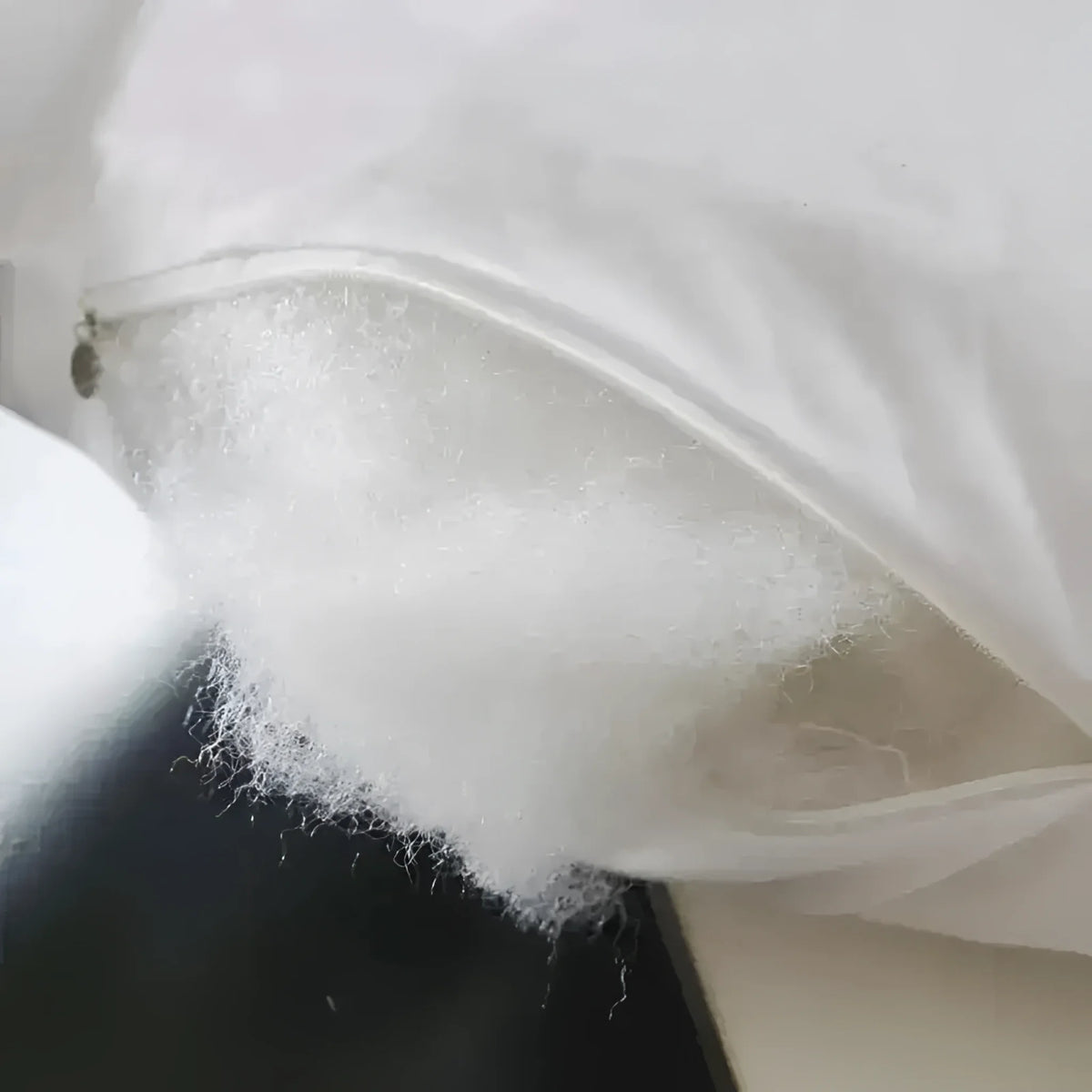 Close-up view of throw pillow filling, showcasing soft white stuffing peeking out from a zippered cover.