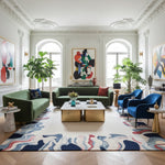 Modern living room with green sofa, a contemporary wool rug, blue chairs, and colorful artwork.