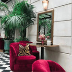 Tiger pattern velvet decorative throw pillow adding a stylish touch to a cozy seating area with red chairs and lush greenery