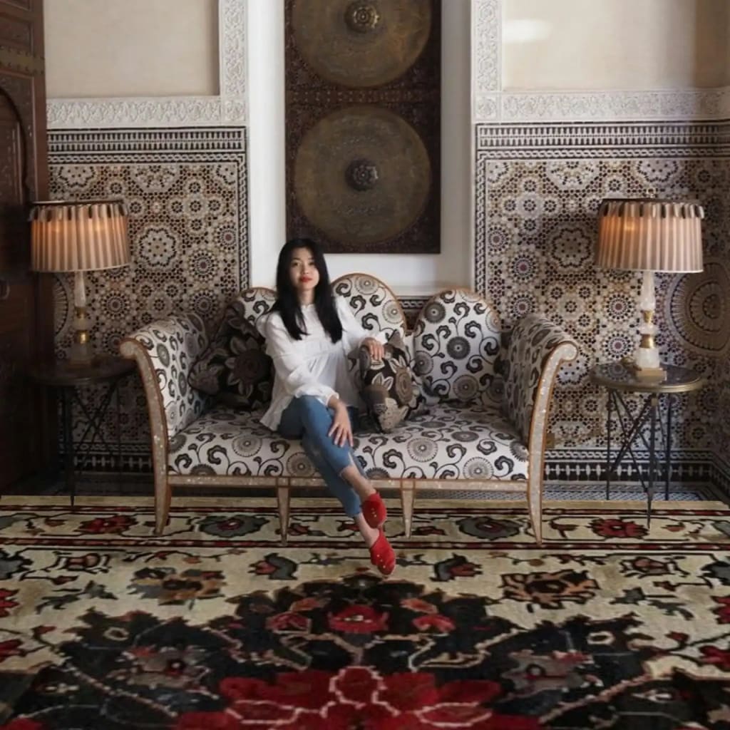 Woman sitting on a patterned sofa in a room with a red hand knotted rug and a large mirror.