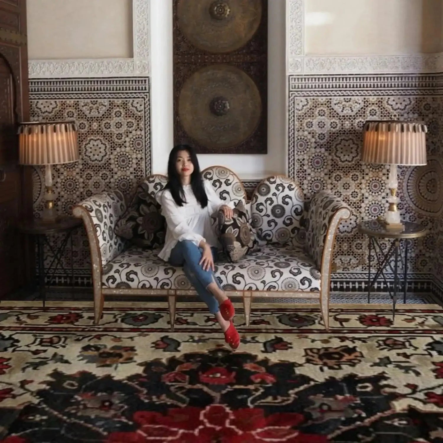 Woman sitting on a patterned sofa in a room with a red hand knotted rug and a large mirror.