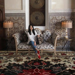 Woman sitting on a patterned sofa in a room with a red hand knotted rug and a large mirror.
