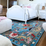 A vibrant blue traditional floral hand-tufted wool rug enhances the cozy ambiance of a living room, placed on a wooden floor beside a white bed. This area rug, perfect for adding warmth and style to any living room, features intricate floral patterns in red, green, and beige, making it a standout piece among rugs for living rooms.