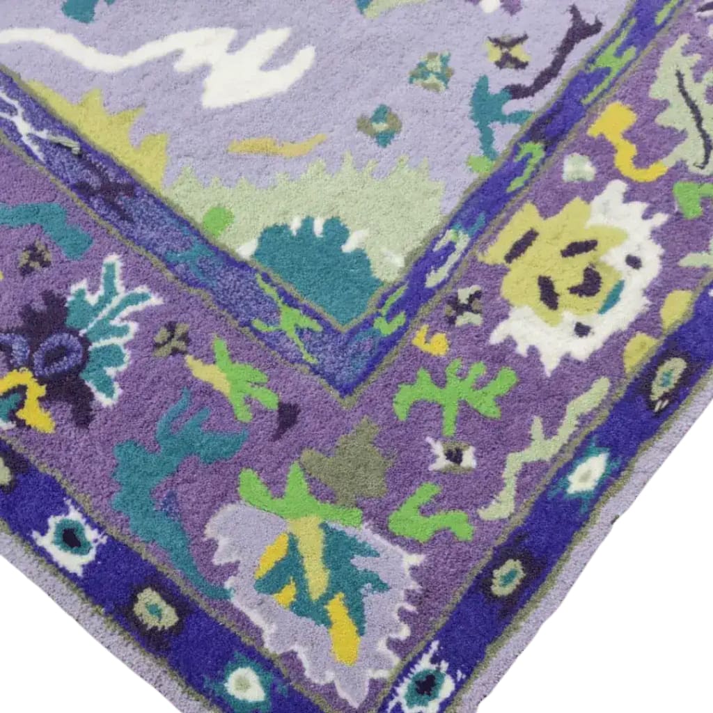 Close-up view of a traditional floral hand tufted wool rug in vibrant purple, showcasing intricate floral patterns with shades of green, yellow, and blue. Perfect for adding a touch of elegance to your living room or office space.