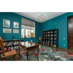 A vibrant living room showcasing the Tranquil Bloom Vista Hand Tufted Area Rug. This wool rug features a stunning floral design with red, yellow, and green hues, perfectly complementing the teal walls and wooden furniture. Ideal for adding a vintage touch to living room spaces or offices, this 8x10 area rug brings elegance and warmth to any setting.