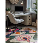 A vibrant area rug with an abstract floral design adds a splash of color to a modern home office. The wool rug complements the large living room space with contemporary flair, featuring a comfortable white chair and a sleek desk against a rustic wall.