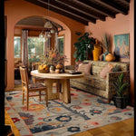 A beautifully decorated living room featuring the Tree of Vibrant Blooms Hand Tufted Area Rug. This wool rug showcases an intricate floral design, adding elegance to the space. Perfect as a living room area rug, its rich colors complement the cozy setting with a stylish sofa, wooden table, and natural light pouring through the windows.