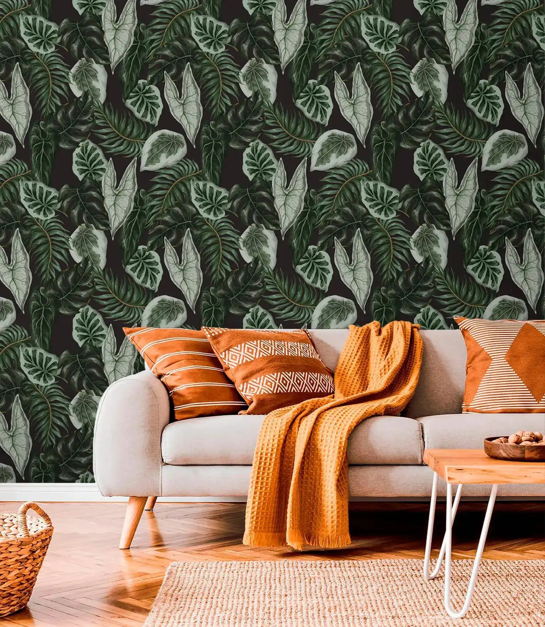 Tropical botanical leaf wallpaper above gray sofa styled with terracotta cushions and amber throw