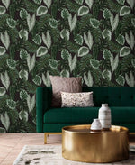 Tropical botanical leaf wallpaper behind emerald velvet sofa and gold drum coffee table