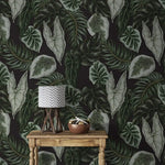 Tropical botanical wallpaper close view, large green leaves on dark wall with rustic table and lamp
