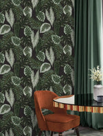 Tropical botanical wallpaper with green leaves on dark ground beside rust chair and sage curtain
