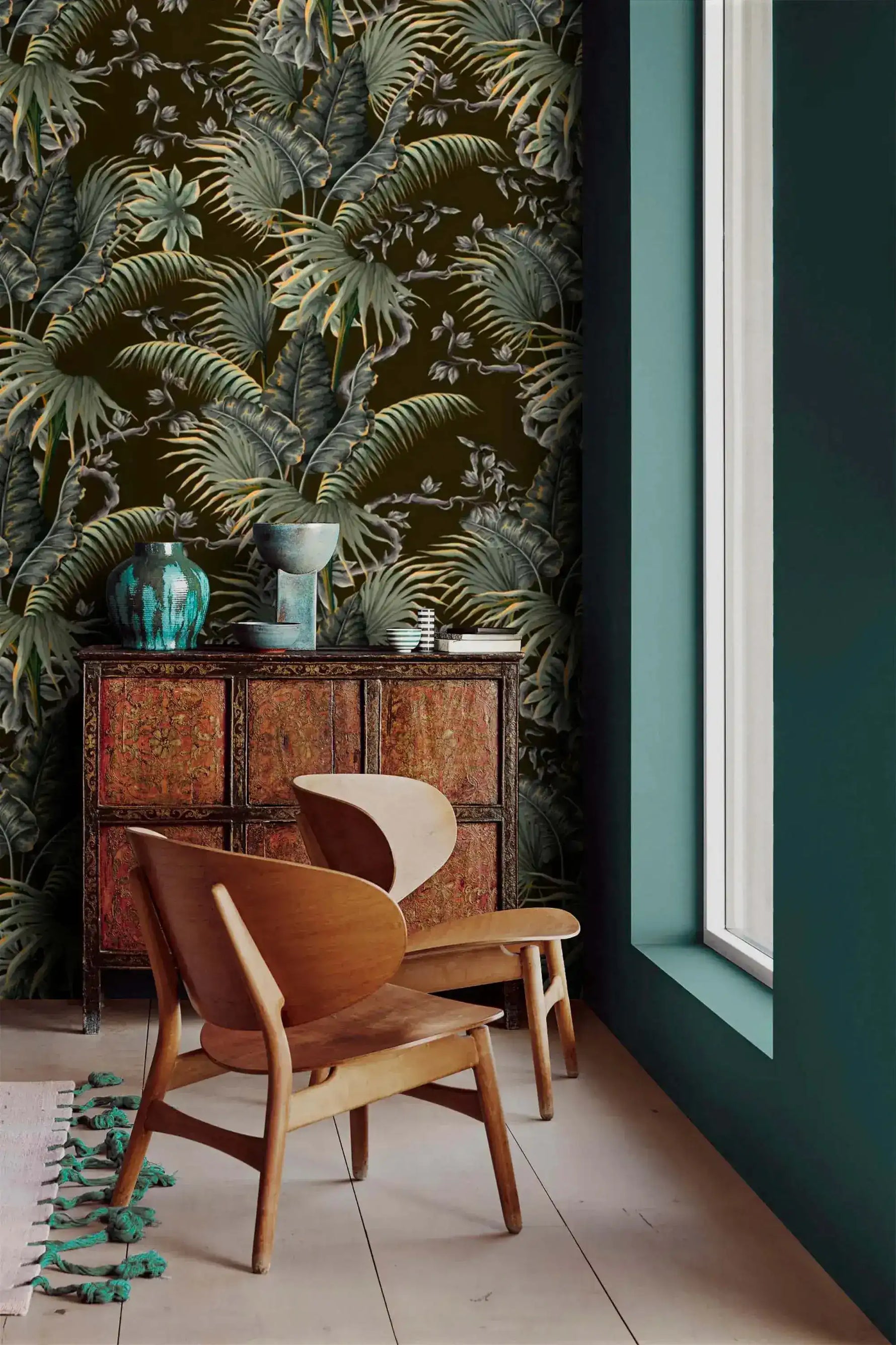 Tropical canopy wallpaper of green palm leaves on dark ground beside a teal wall and carved wood cabinet
