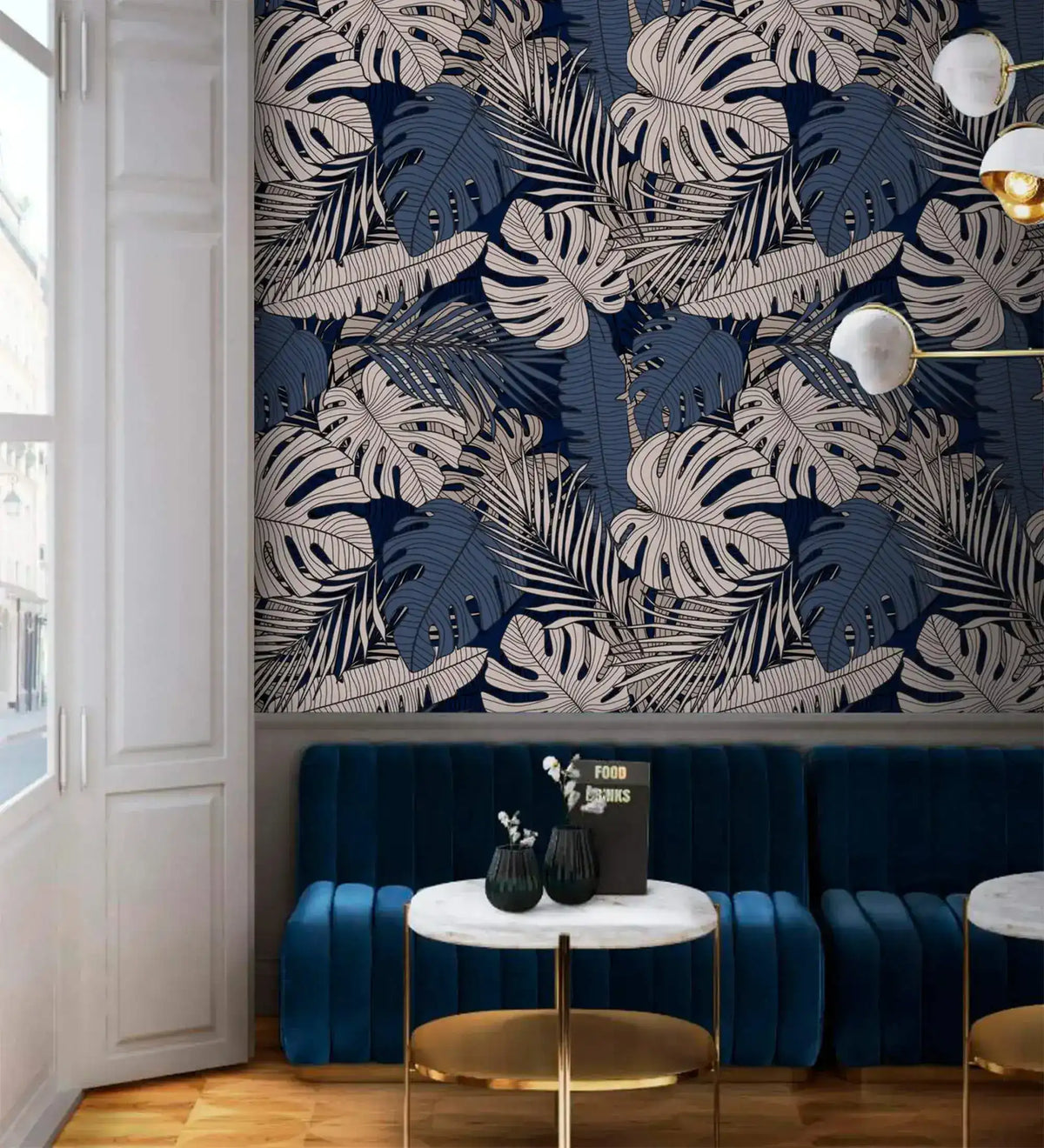 Tropical midnight leaves wallpaper with white monstera and palm fronds on navy, styled in a lounge with blue velvet seating