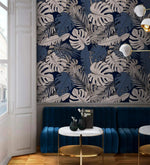 Tropical midnight leaves wallpaper with white monstera and palm fronds on navy, styled in a lounge with blue velvet seating