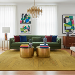 Modern living room with a green sofa, a contemporary yellow rug, a gold coffee tables, and colorful artwork.