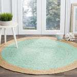 A beautiful turquoise round jute rug is elegantly placed on a wooden floor, near a white side table with a plant and decorative items. This area rug is perfect for adding a touch of style to dining rooms or living rooms, enhancing any space with its natural texture and vibrant color.
