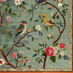 A beautifully detailed wool rug featuring a nature-inspired design with birds perched on flowering branches. This square area rug, perfect for a dining room or living room, showcases a rich floral motif with vibrant colors, ideal for formal settings. The large area rug adds an elegant touch to any space.