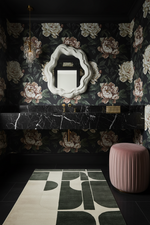 Bathroom with floral wallpaper, marble vanity, green rug, and pink stool.