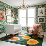 Nursery room with green patterned wallpaper, floral rug, and pink chair.