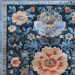 Close-up view of the Verdant Tapestry Hand Tufted Rug, showcasing intricate floral patterns in soft blues, creams, and oranges against a dark background. Ideal for adding a vintage touch to dining room areas, this wool area rug blends beautifully with classic décor.