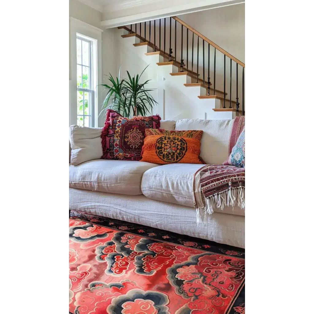 A vibrant Vermilion Cloud Frame Hand Tufted Area Rug elegantly placed in a cozy living room. The large wool rug features an abstract design with rich red and black hues, complementing the white sofa adorned with colorful cushions. Perfect for adding warmth and style to large living room spaces.
