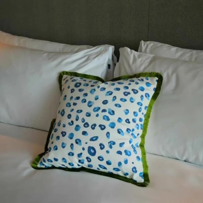 Vibrant throw pillow featuring an aquatic leopard print design with blue spots on a white background and a green fringe trim, perfect for adding a pop of color to any living space.